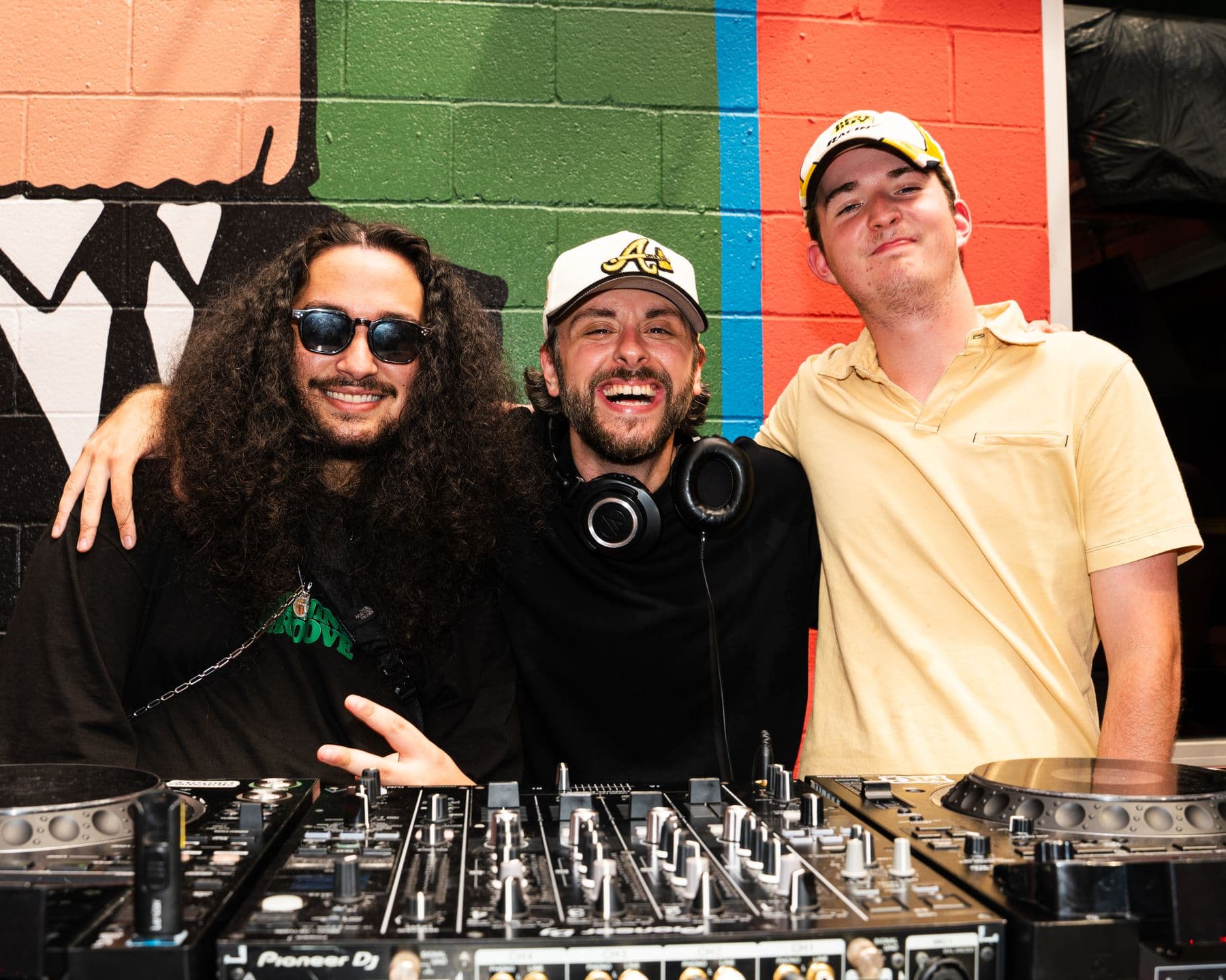 Three DJs at the decks under the paper-bag mural